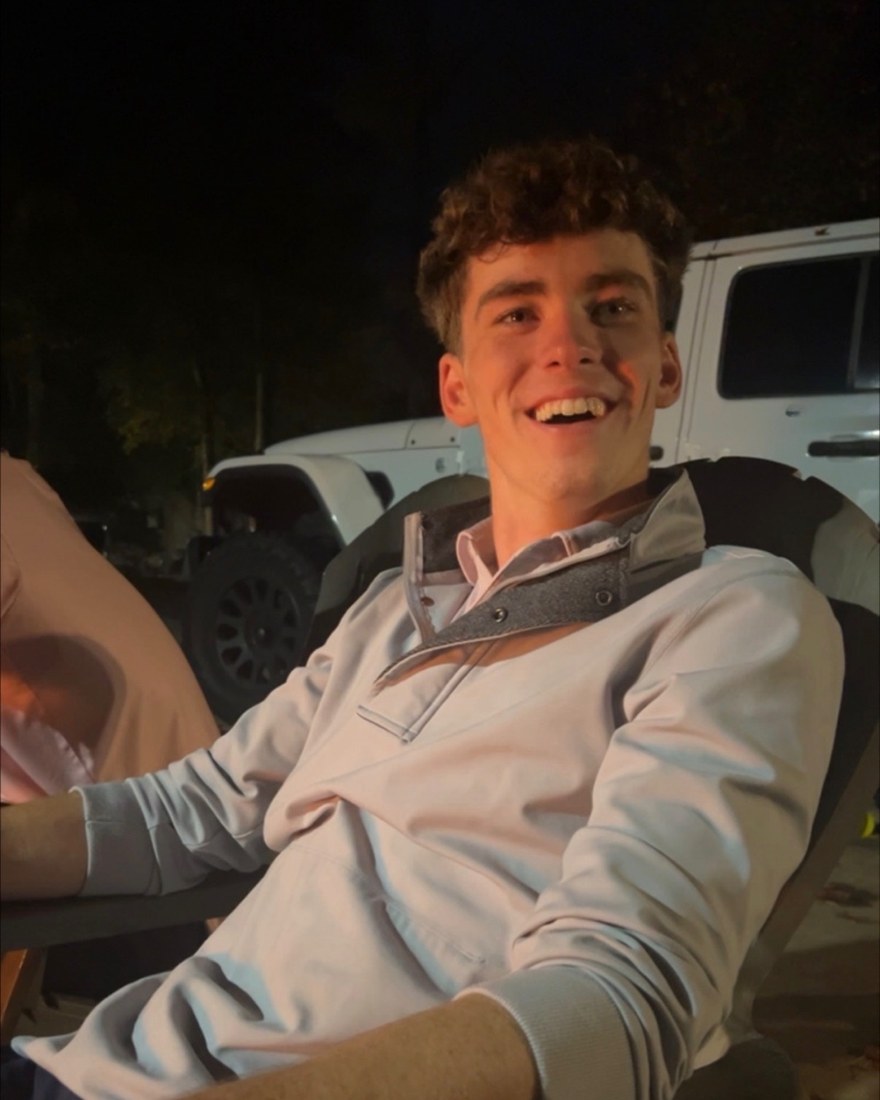 Jimmy Gracey, seated in a folding chair outdoors at night, smiling at the camera.